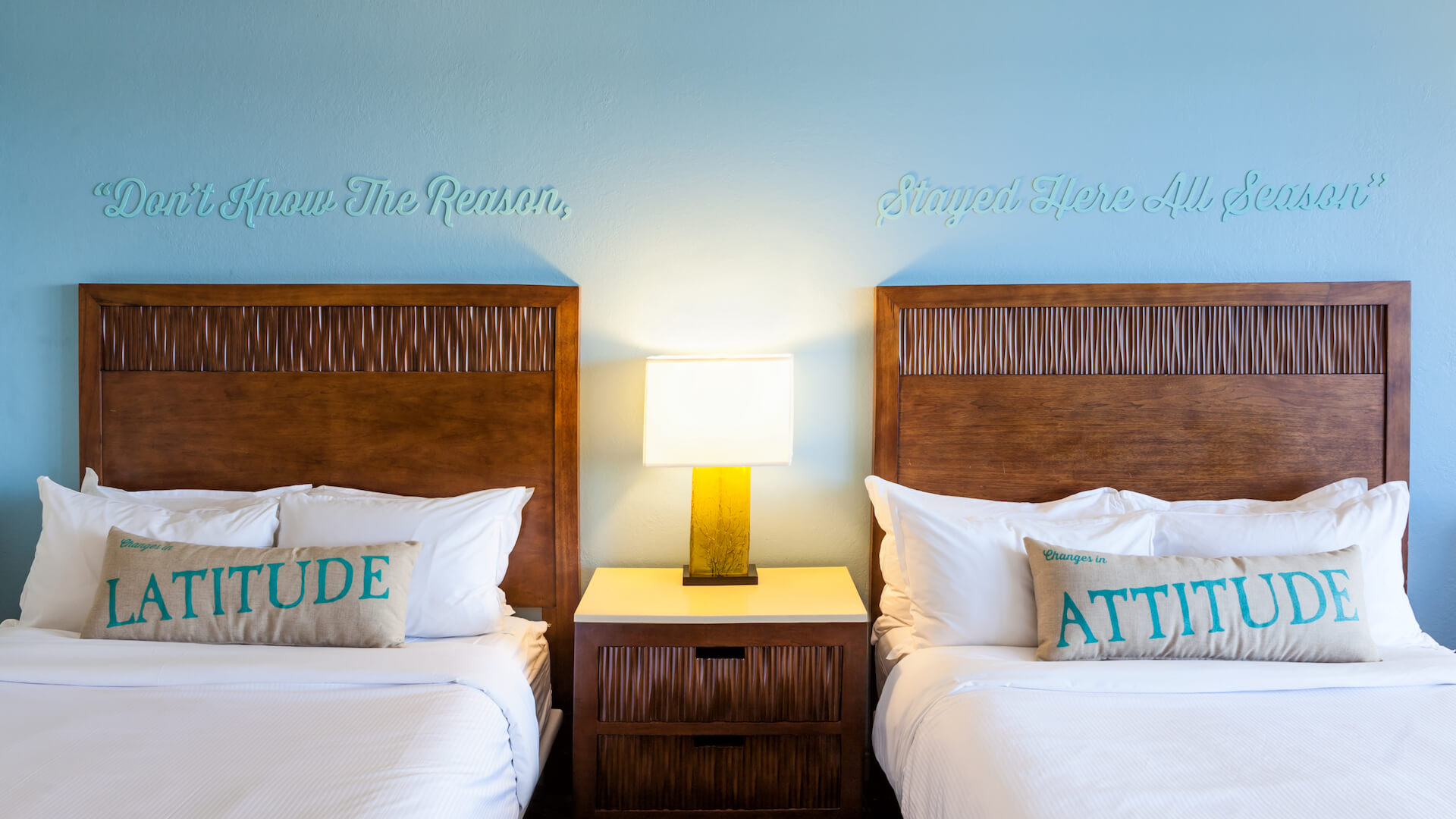Two beds with pillows and end table with lamp in the middle